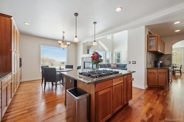 kitchen with stainless steel gas cooktop, a kitchen island, brown cabinetry, glass insert cabinets, and pendant lighting