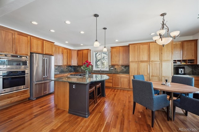 kitchen with stainless steel appliances, a center island, dark stone counters, and hanging light fixtures