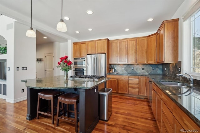 kitchen featuring a kitchen island, a sink, appliances with stainless steel finishes, dark stone countertops, and dark wood finished floors