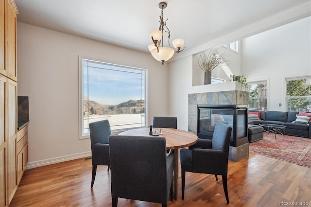 dining room featuring light wood-type flooring, a fireplace, baseboards, and a chandelier