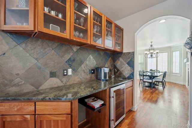 kitchen featuring glass insert cabinets, beverage cooler, brown cabinets, dark stone counters, and decorative light fixtures