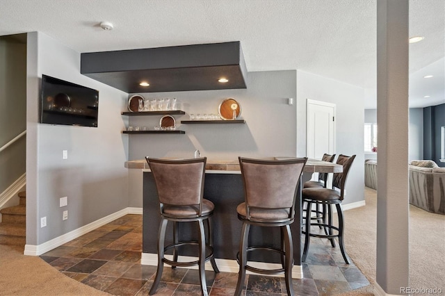 bar with a textured ceiling, bar area, baseboards, stairs, and dark carpet