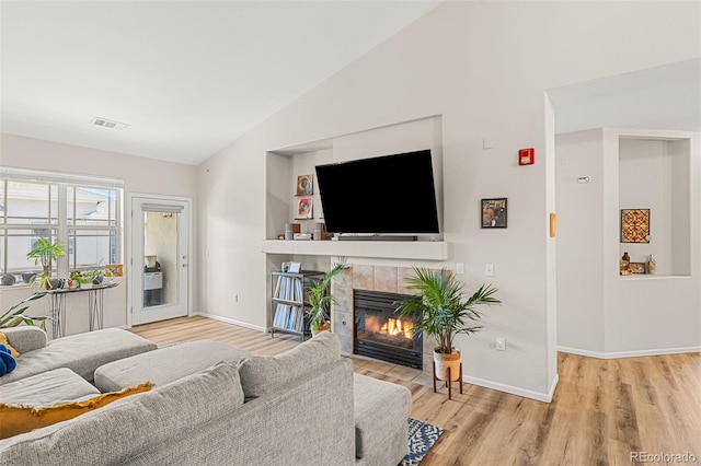 living room featuring visible vents, a fireplace, wood finished floors, baseboards, and lofted ceiling