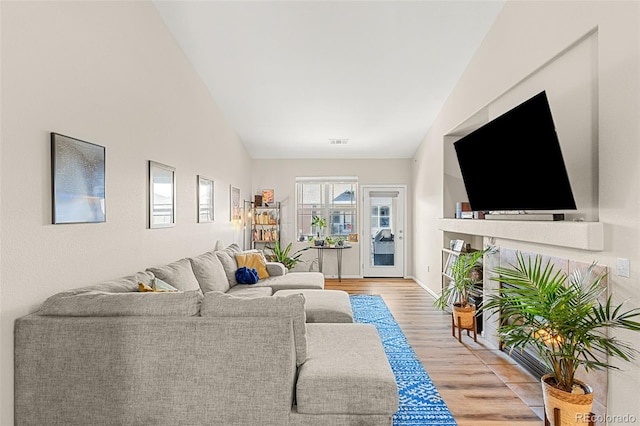 living area featuring light wood-style floors, baseboards, visible vents, and lofted ceiling