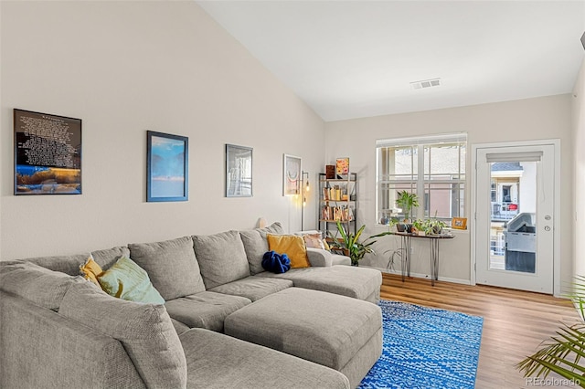 living area featuring baseboards, high vaulted ceiling, wood finished floors, and visible vents