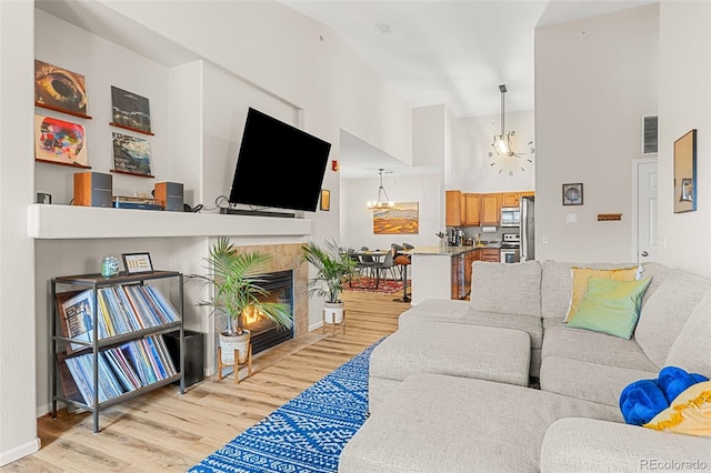 living room with visible vents, light wood-type flooring, a tile fireplace, a notable chandelier, and a high ceiling