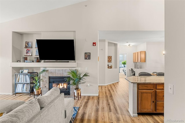 living area featuring baseboards, light wood-type flooring, a tile fireplace, and lofted ceiling