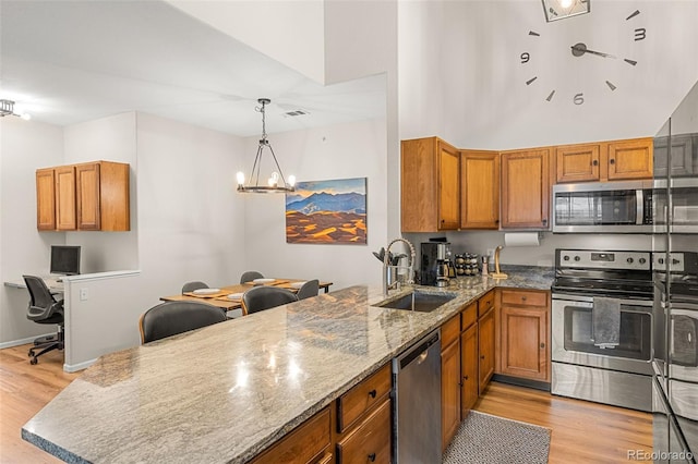 kitchen featuring a peninsula, appliances with stainless steel finishes, a sink, and light wood-type flooring