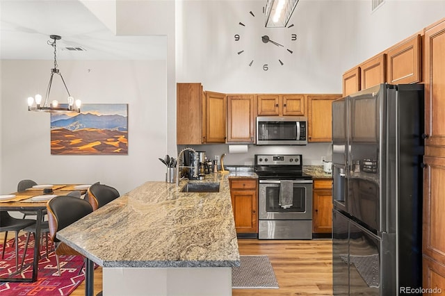 kitchen with brown cabinetry, appliances with stainless steel finishes, light wood-type flooring, a peninsula, and a breakfast bar