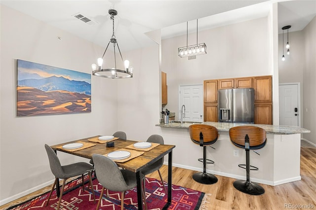 dining space featuring a chandelier, a high ceiling, visible vents, and light wood-style flooring