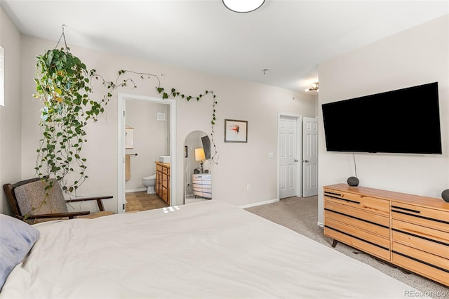 bedroom featuring arched walkways, baseboards, light colored carpet, and ensuite bath