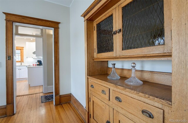 hallway with light wood-style flooring, baseboards, and crown molding