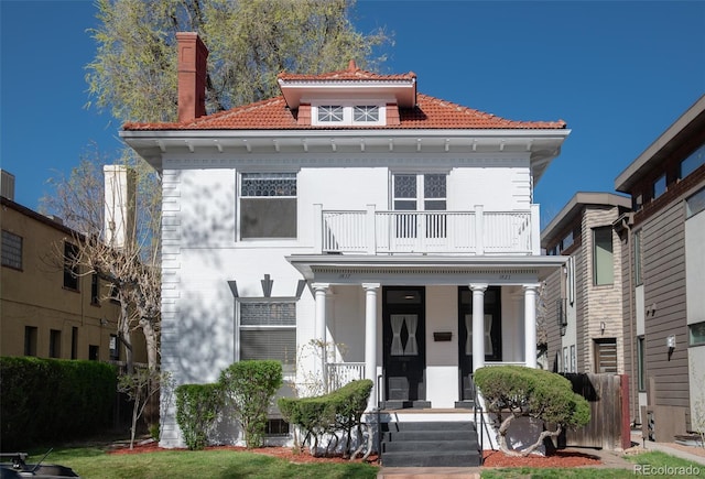 view of front of house with a balcony, a tiled roof, a porch, and a chimney
