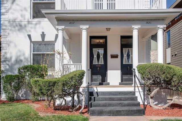 property entrance with a balcony, brick siding, and a porch