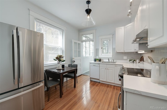 kitchen with stainless steel appliances, wall chimney range hood, white cabinets, and light countertops