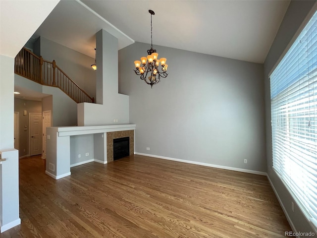 unfurnished living room featuring hardwood / wood-style floors, a notable chandelier, lofted ceiling, and a healthy amount of sunlight