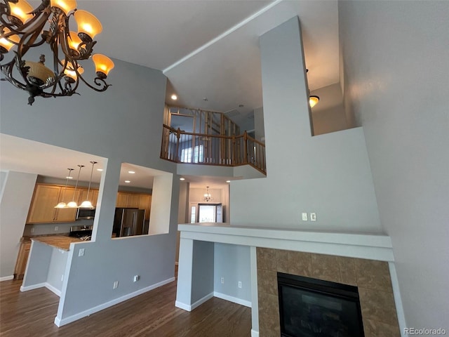 unfurnished living room featuring a fireplace, a high ceiling, dark hardwood / wood-style flooring, and a chandelier