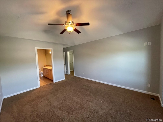 unfurnished bedroom featuring ensuite bath, ceiling fan, and dark carpet