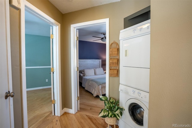 clothes washing area with ceiling fan, stacked washing maching and dryer, and light hardwood / wood-style flooring