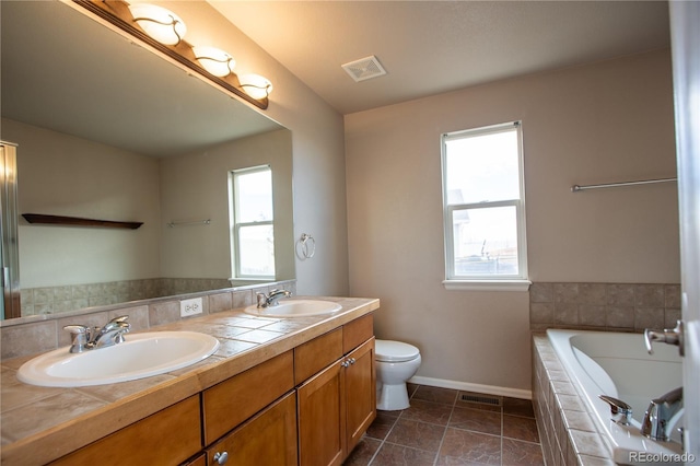 bathroom featuring a relaxing tiled tub, vanity, toilet, and a wealth of natural light