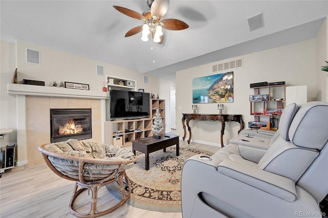 living room featuring a tiled fireplace, ceiling fan, and light hardwood / wood-style floors