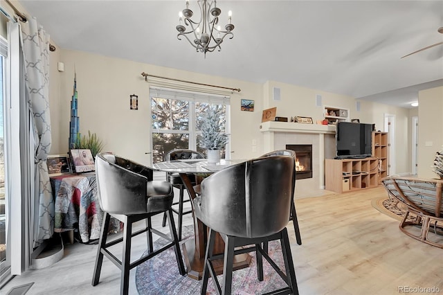 dining room with a tiled fireplace, ceiling fan with notable chandelier, and light wood-type flooring