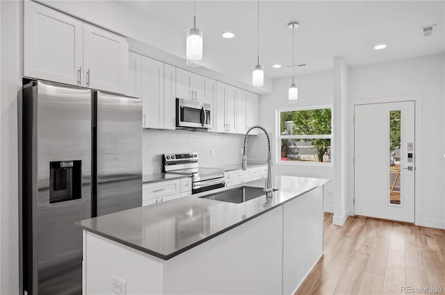 kitchen featuring pendant lighting, white cabinets, sink, an island with sink, and appliances with stainless steel finishes