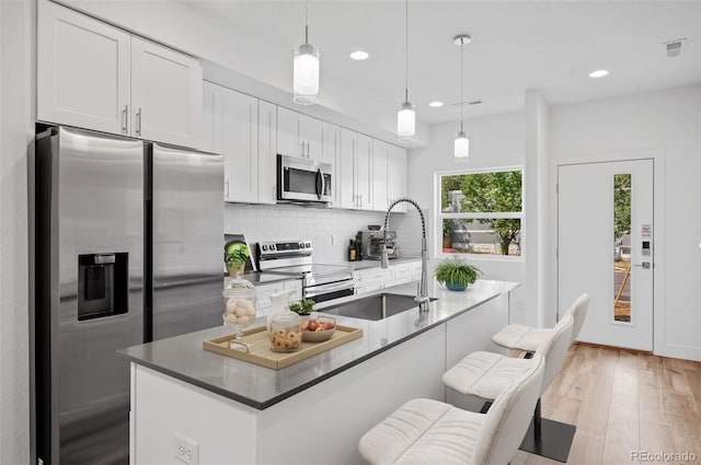 kitchen with light wood-type flooring, stainless steel appliances, sink, decorative light fixtures, and white cabinetry