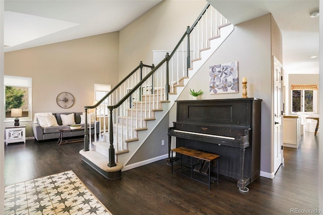 stairway with a wealth of natural light, a towering ceiling, baseboards, and wood finished floors