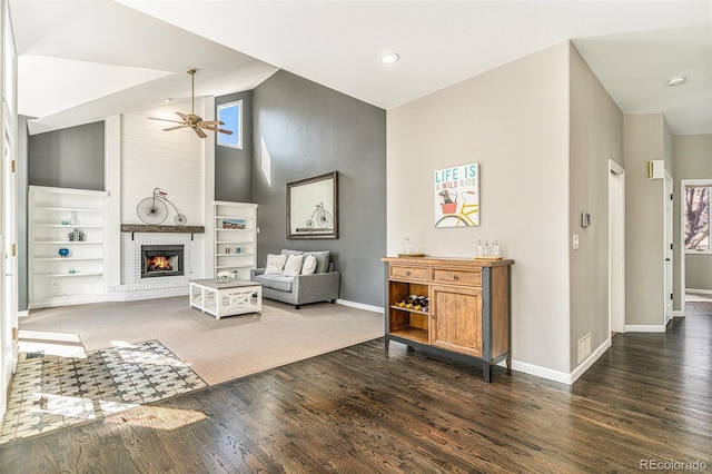 living area featuring a brick fireplace, baseboards, dark wood-style floors, high vaulted ceiling, and a ceiling fan