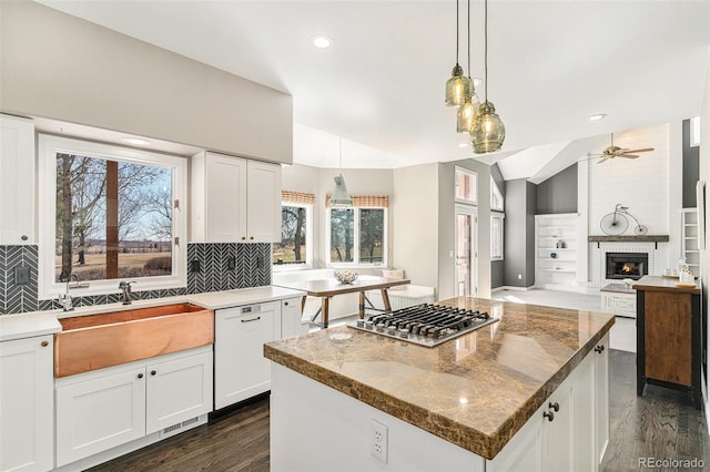 kitchen featuring stainless steel gas cooktop, white dishwasher, a sink, vaulted ceiling, and a brick fireplace