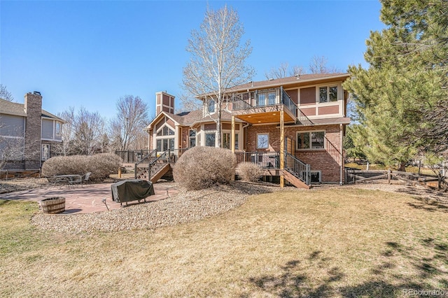 rear view of house featuring a balcony, stairs, a lawn, a patio area, and brick siding