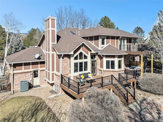 rear view of house with central AC unit, a shingled roof, a chimney, a deck, and brick siding