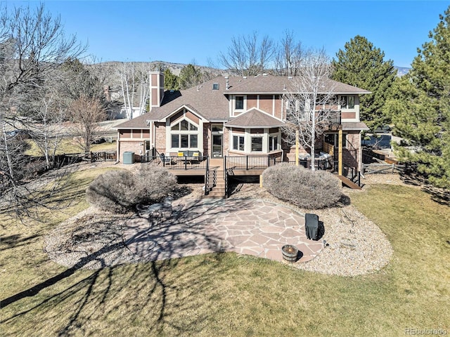 rear view of property featuring a lawn, a deck, a patio, brick siding, and a chimney