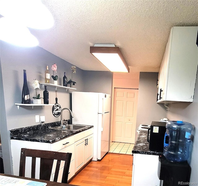 kitchen featuring white cabinetry, sink, light hardwood / wood-style flooring, white refrigerator, and a textured ceiling