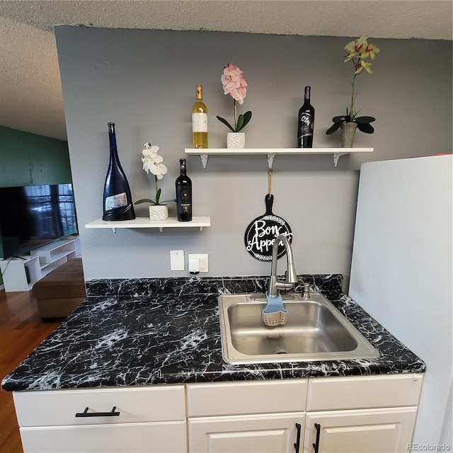 room details featuring a textured ceiling, white fridge, white cabinetry, and sink