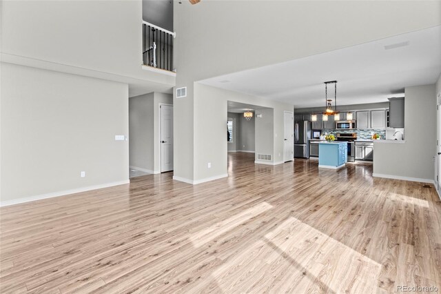 8414 Bed Straw St, Parker, CO 80134 - unfurnished living room featuring light wood-style floors, baseboards, a chandelier, a high ceiling, and a sink