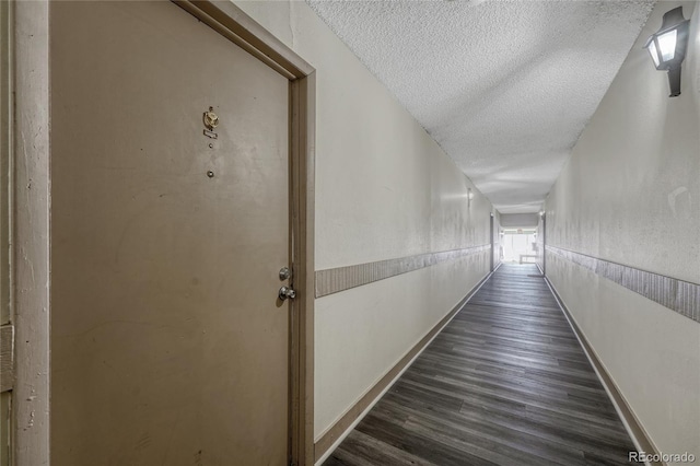 corridor featuring a wainscoted wall, baseboards, dark wood-type flooring, and a textured ceiling