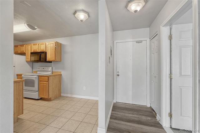 kitchen featuring light countertops, white electric range, light brown cabinets, black microwave, and baseboards