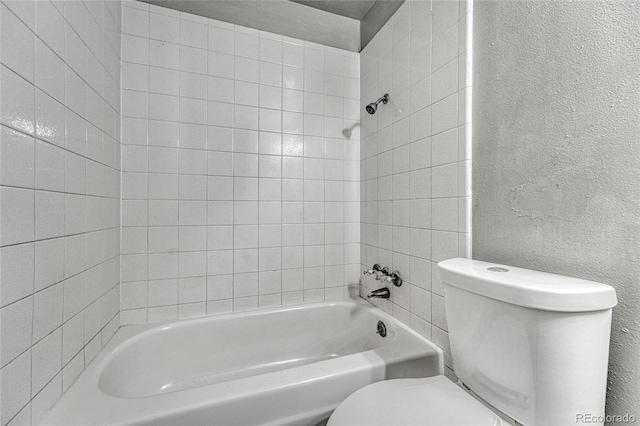 bathroom with toilet, shower / tub combination, and a textured wall