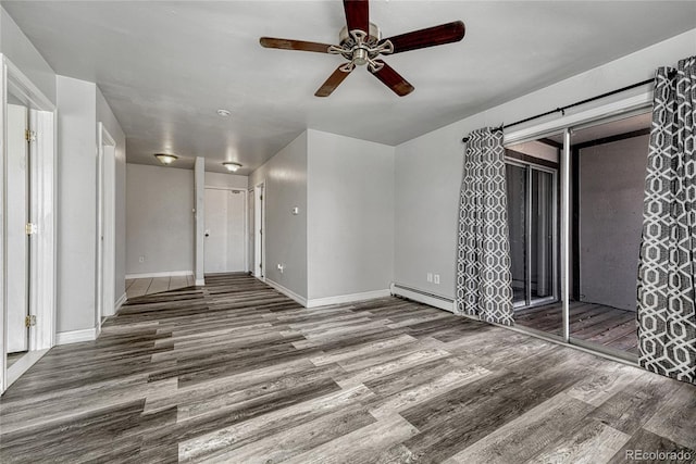 spare room featuring a baseboard radiator, a barn door, a ceiling fan, wood finished floors, and baseboards