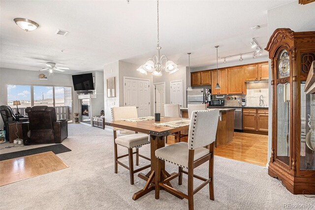 dining area with ceiling fan with notable chandelier, a lit fireplace, visible vents, and light colored carpet