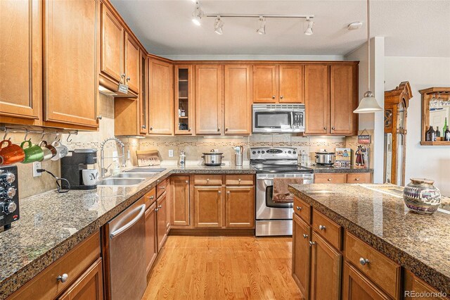 kitchen with light wood finished floors, stainless steel appliances, brown cabinetry, glass insert cabinets, and a sink