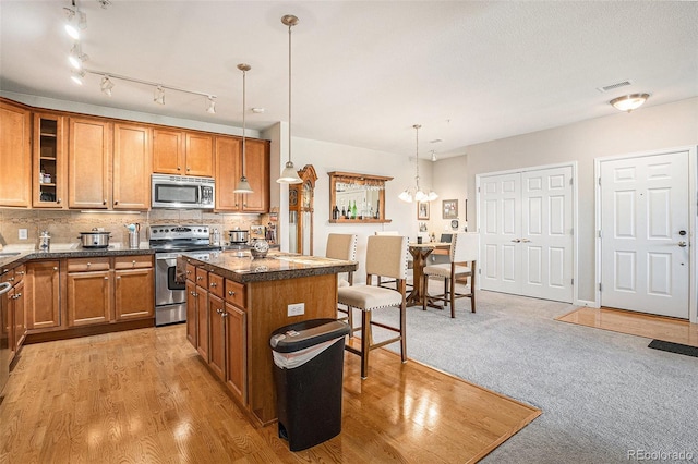 kitchen with stainless steel appliances, decorative backsplash, brown cabinetry, a kitchen island, and a kitchen bar