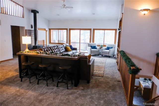 living room with baseboards, high vaulted ceiling, a wood stove, ceiling fan, and dark colored carpet