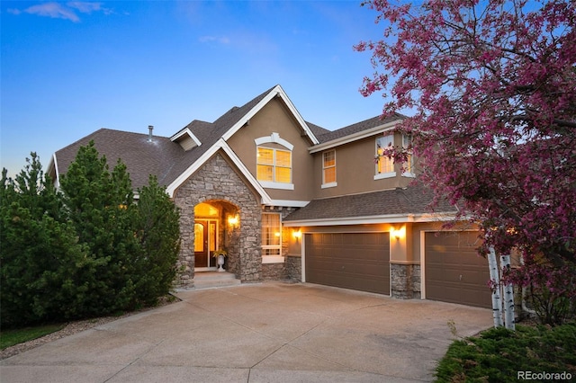 view of front of property with an attached garage, driveway, stone siding, and stucco siding