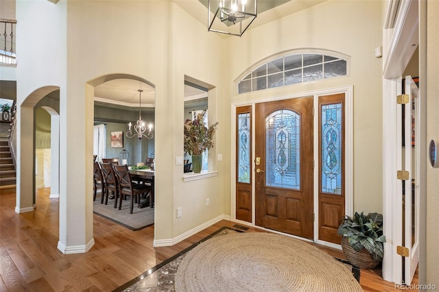 foyer featuring an inviting chandelier, wood finished floors, baseboards, a high ceiling, and arched walkways