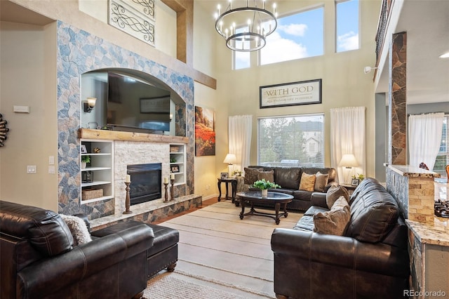living area featuring plenty of natural light, a stone fireplace, wood finished floors, and a chandelier