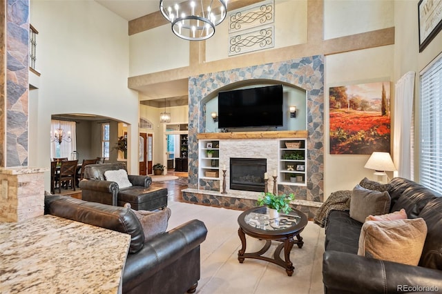 living area featuring an inviting chandelier, a glass covered fireplace, a high ceiling, and built in shelves