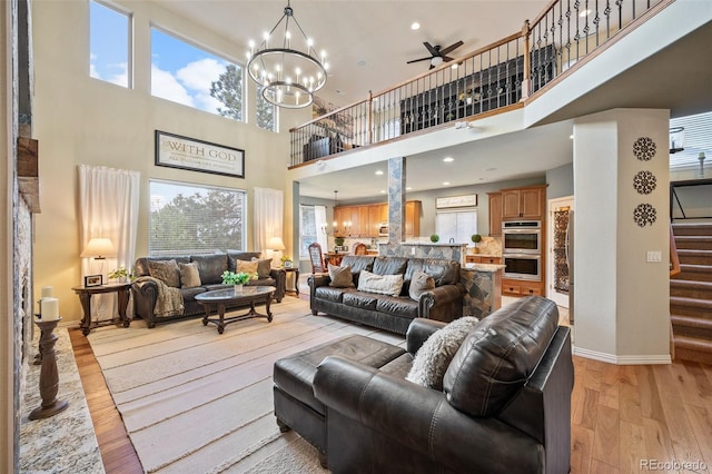 living area featuring a towering ceiling, baseboards, stairway, light wood-type flooring, and ceiling fan with notable chandelier